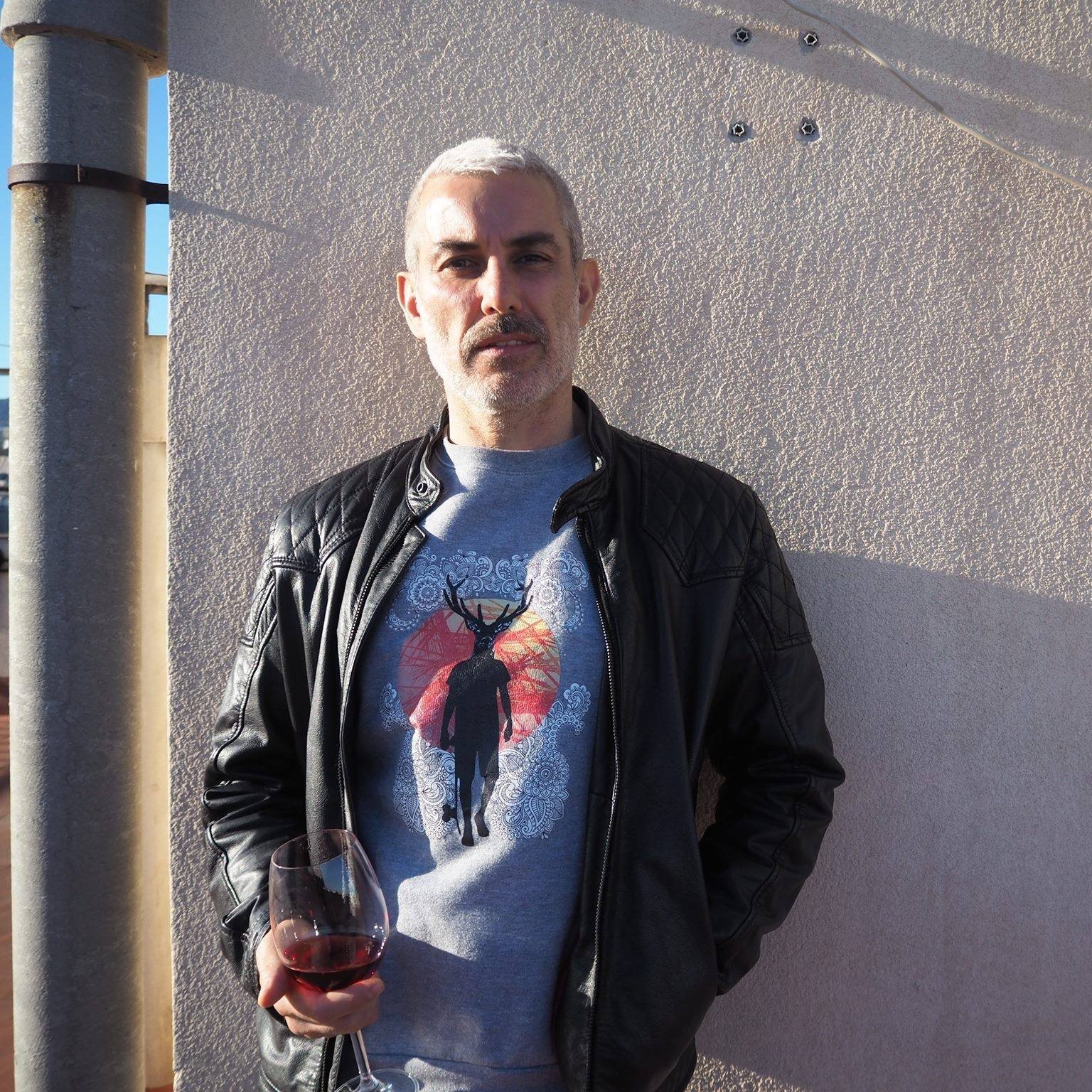 Michael Salverda against a sunlit wall, holding a glass of red wine
